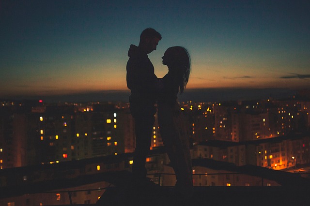 Muž a žena v objatí stoja na streche nad vysvieteným nočným mestom.jpg